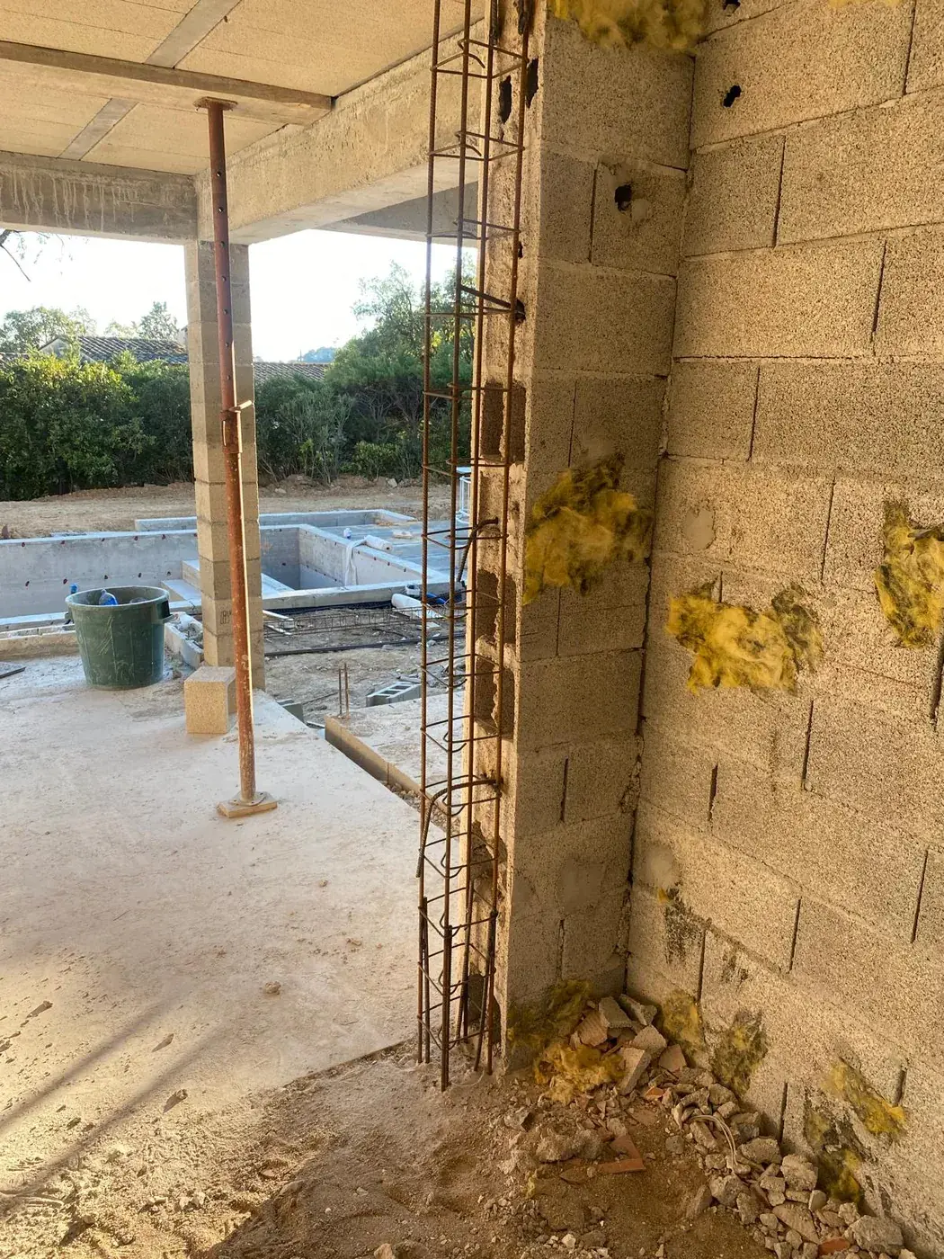 Cage d'armatures le long d'un mur en parpaings, piscine en construction au fond