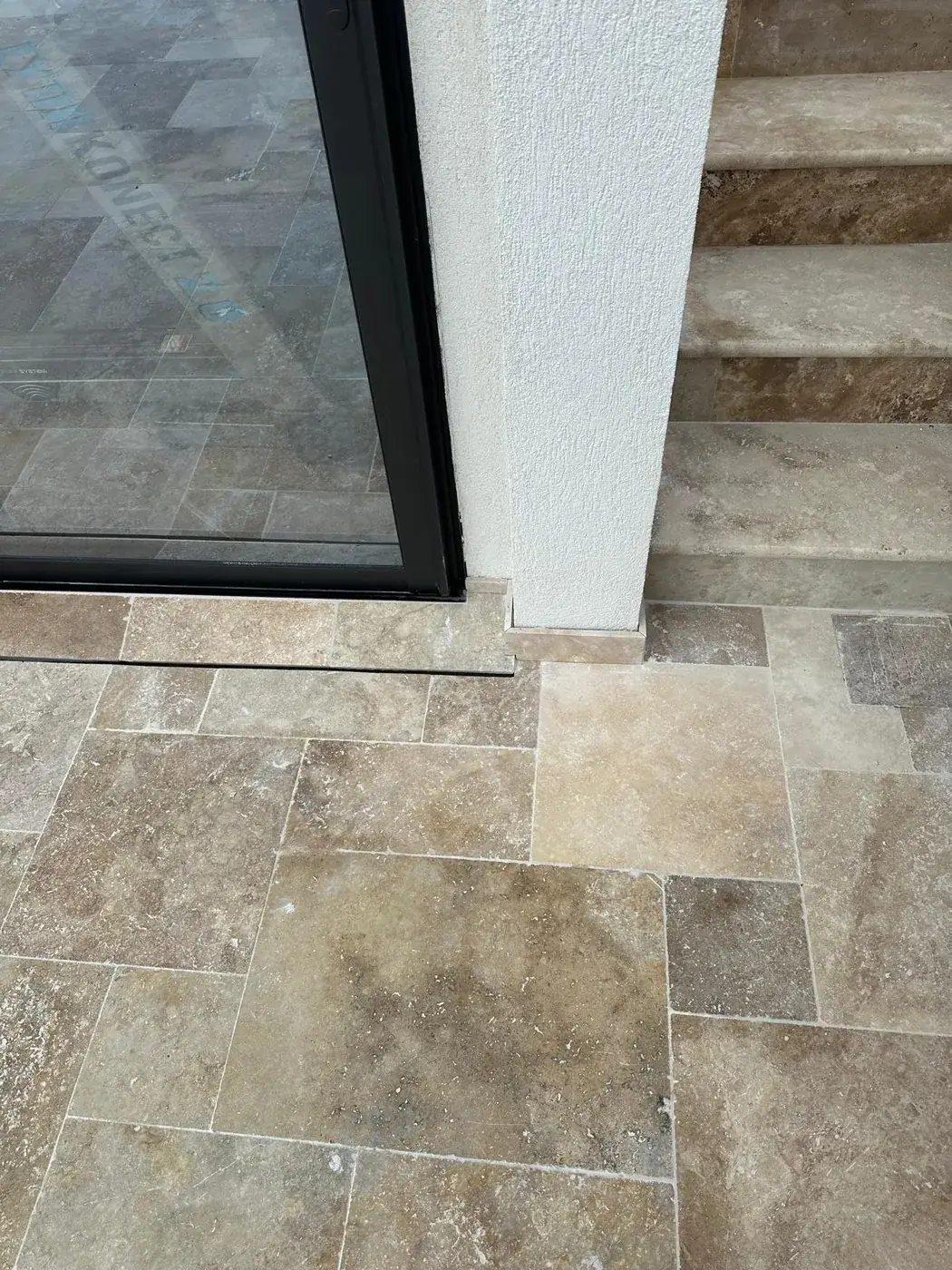 Emmarchement en travertin devant une menuiserie aluminium noire