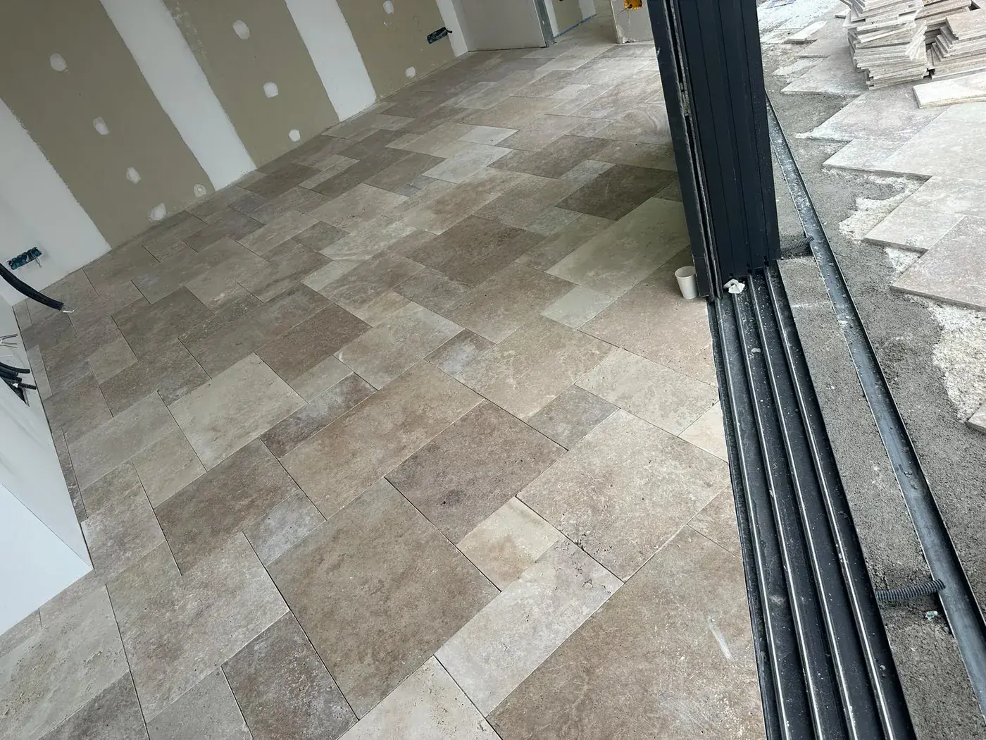 Terrasse intérieure-extérieure en travertin devant de grandes menuiseries noires