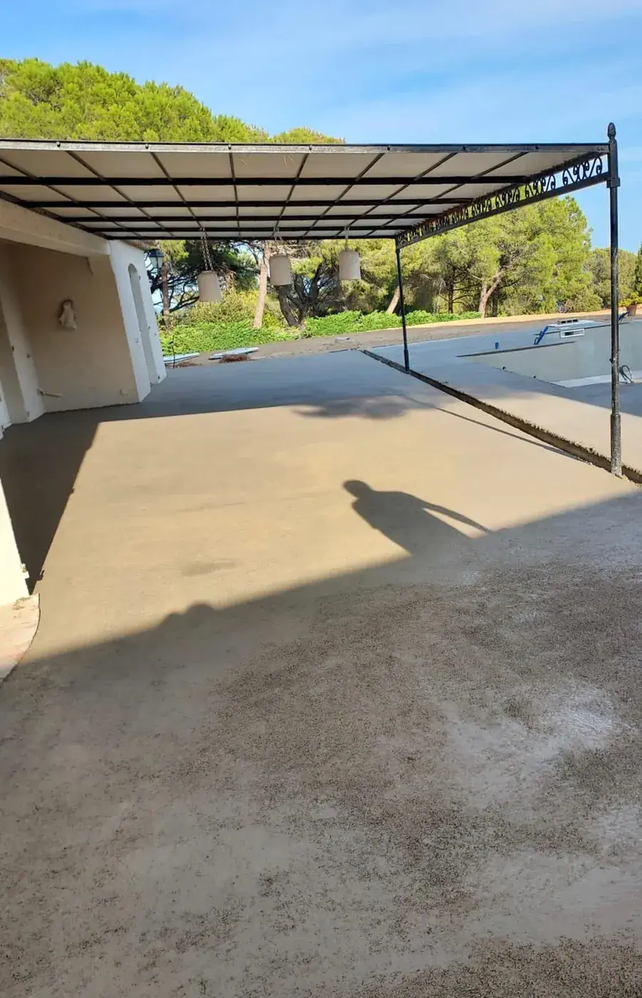 Chape terminée sous la pergola métallique, piscine à droite