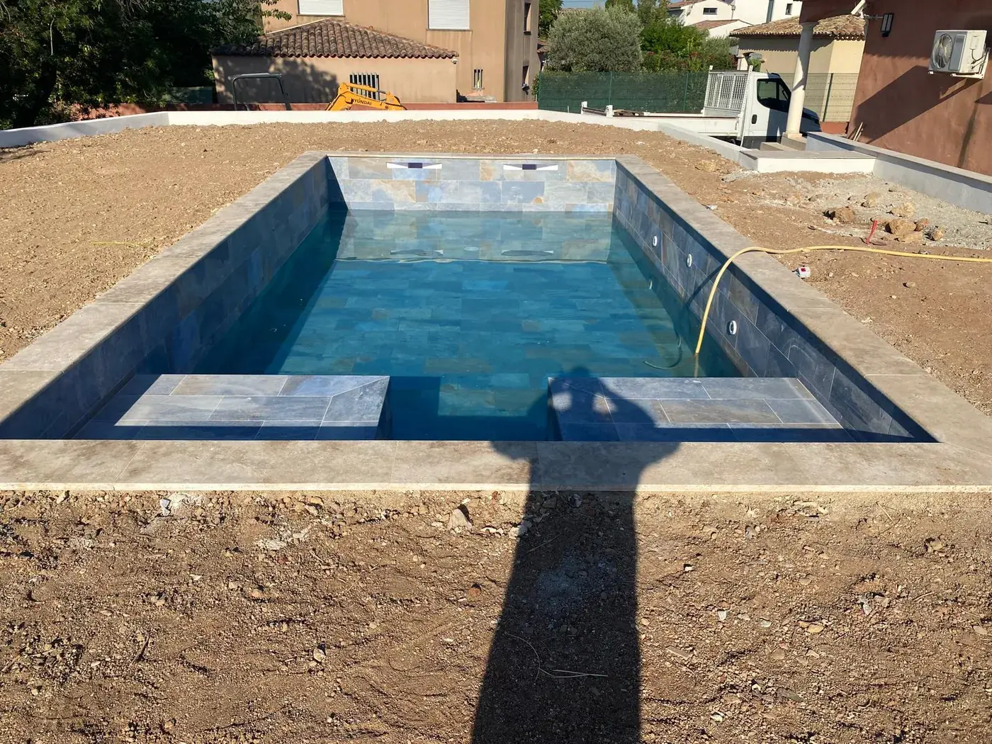 Piscine béton terminée et mise en eau, carrelage effet pierre et margelles