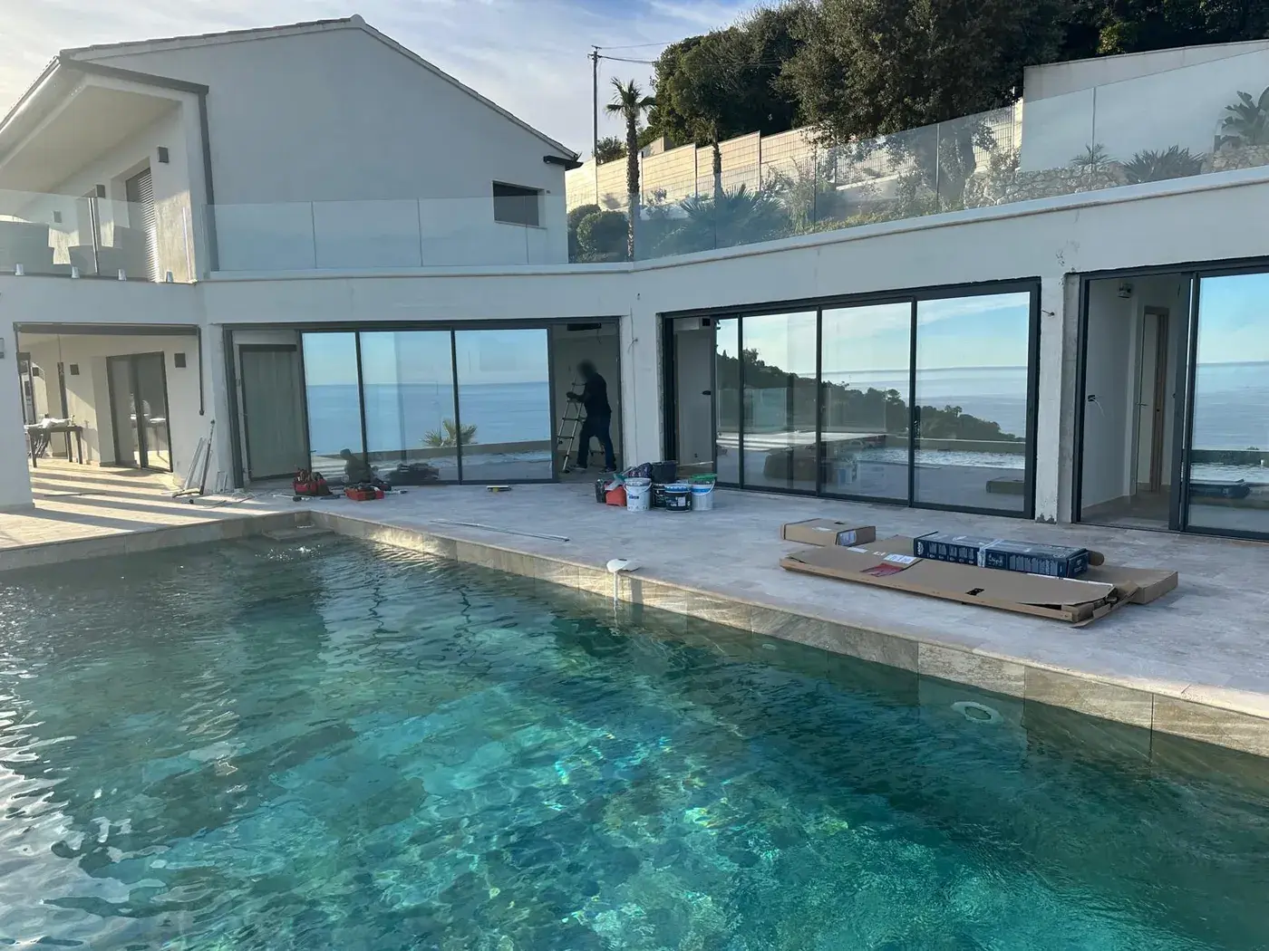 Terrasse en travertin et piscine à débordement d'une villa contemporaine face à la mer